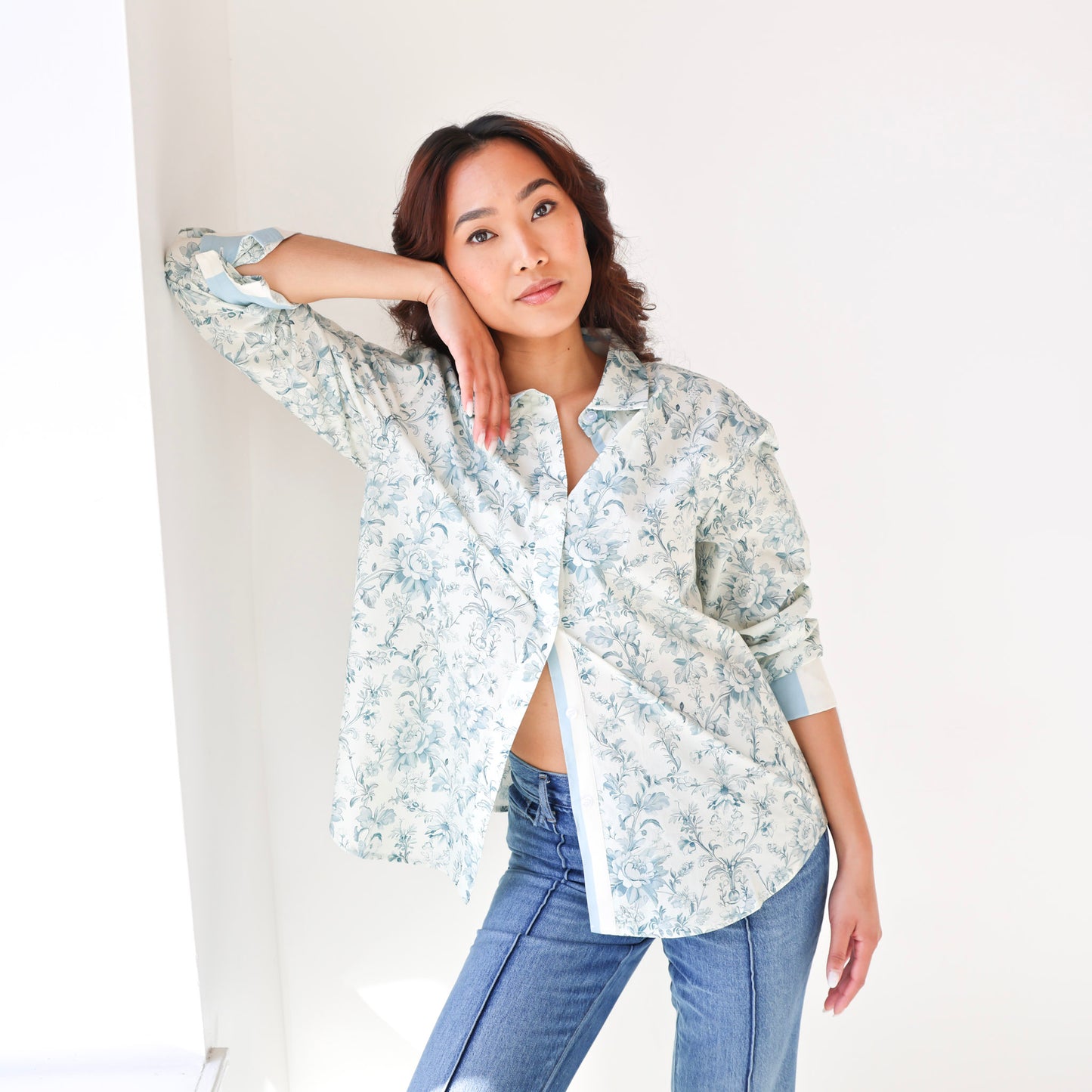 Woman wearing a floral shirt and jeans against a white background