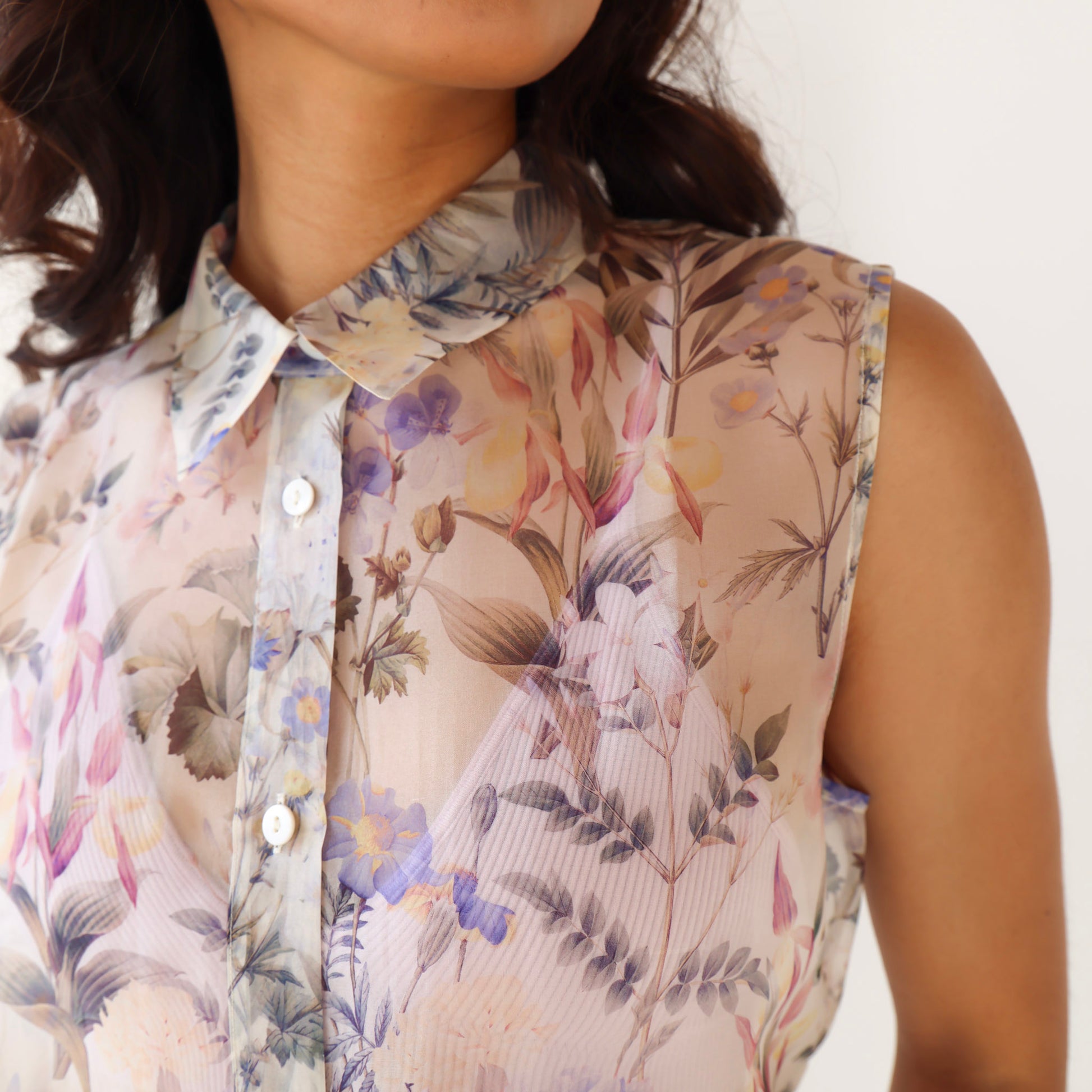 Close-up of a person wearing a sleeveless floral blouse with a blurred background
