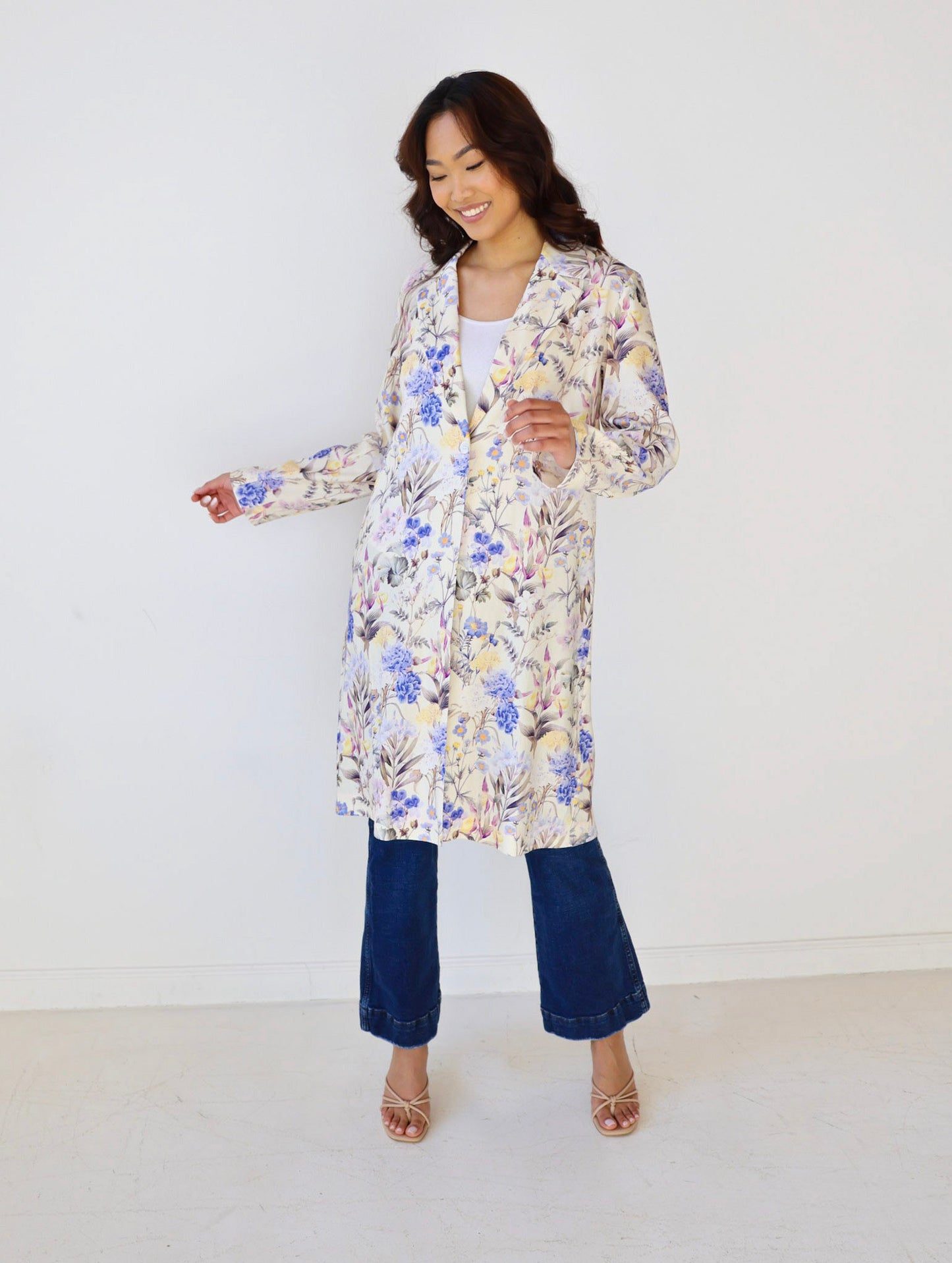 Woman wearing a floral dress over a white shirt with blue jeans on a white background