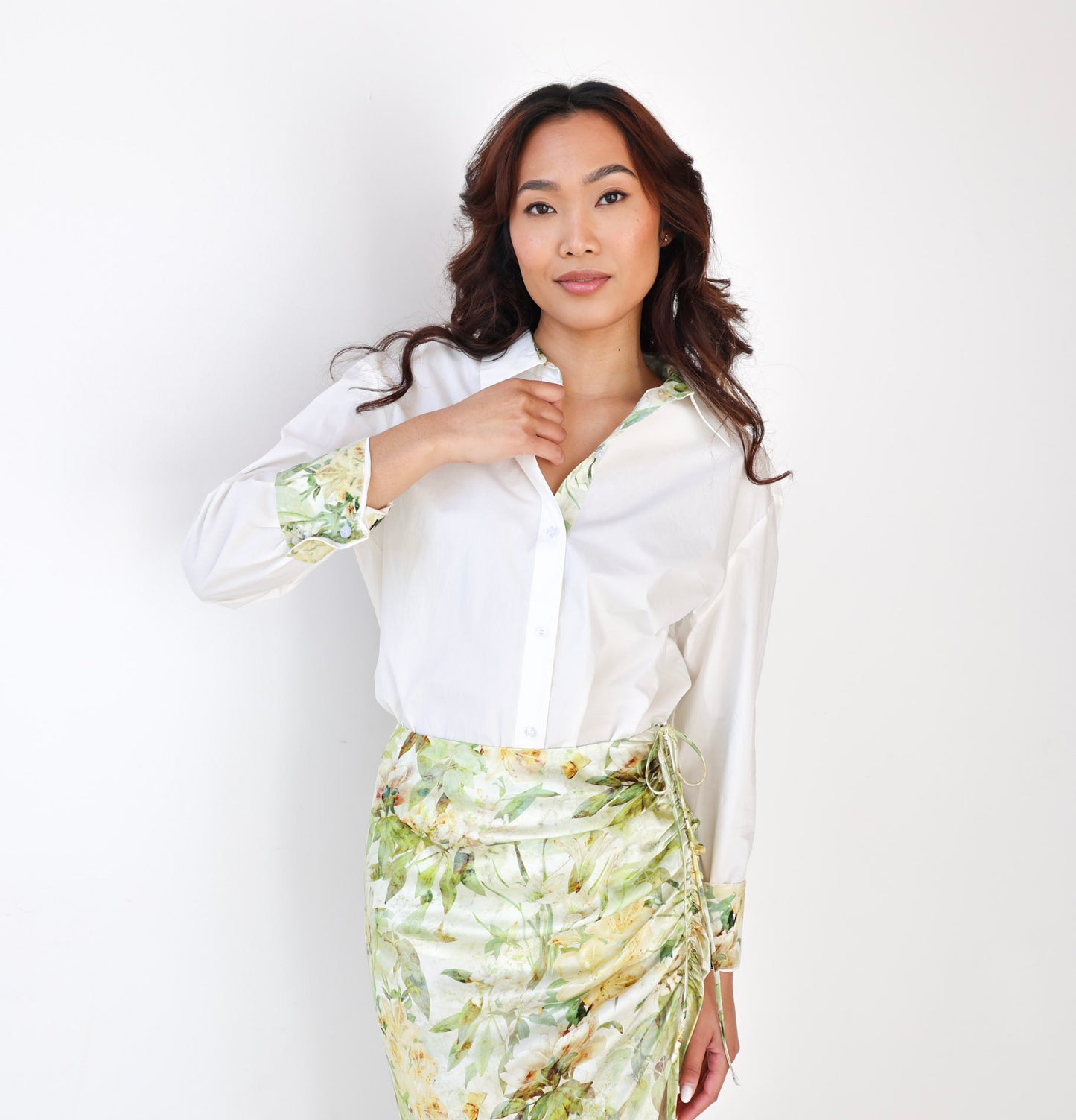 Woman wearing a white blouse with floral cuffs and a green floral skirt against a white background