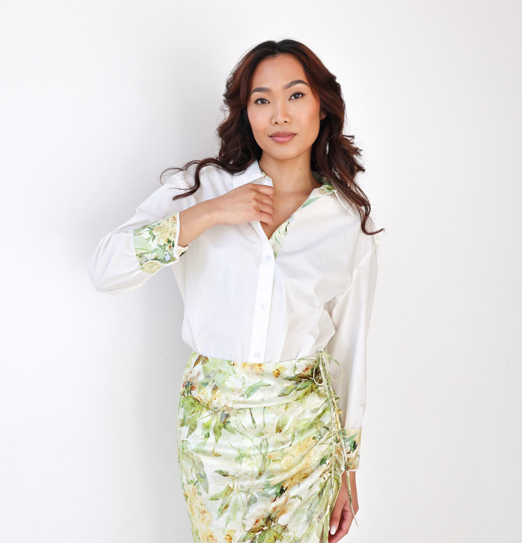 Woman wearing a white blouse with floral cuffs and a green floral skirt against a white background